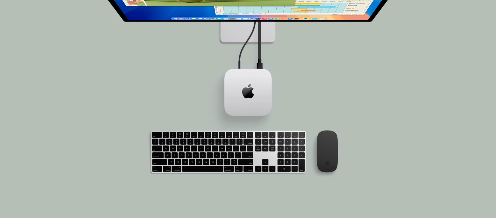 Pohled shora na st?íbrny Mac mini p?ipojeny k monitoru, na kterém je rozehraná hra, vedle jsou bezdrátová klávesnice, herní ovlada? a modré AirPody Max