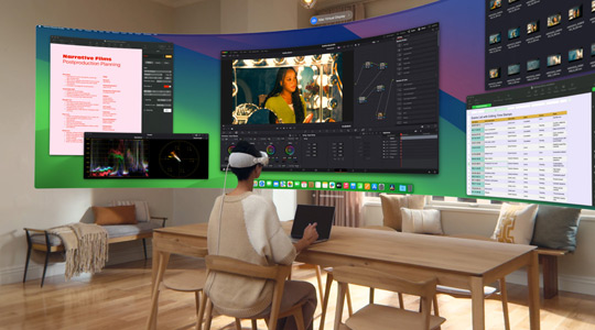 Une personne portant l’Apple Vision Pro est assise à un bureau avec un MacBook Pro 13 pouces ouvert ; un affichage incurvé et ultra grand?angle de son écran est projeté dans la pièce