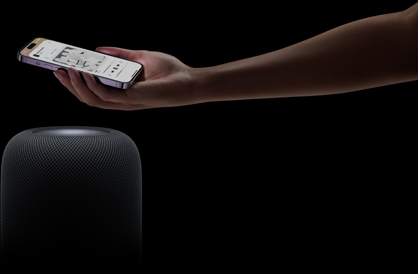 一隻手從頁(yè)面右側(cè)而來(lái)，在 HomePod 揚(yáng)聲器上方拿著一部 iPhone