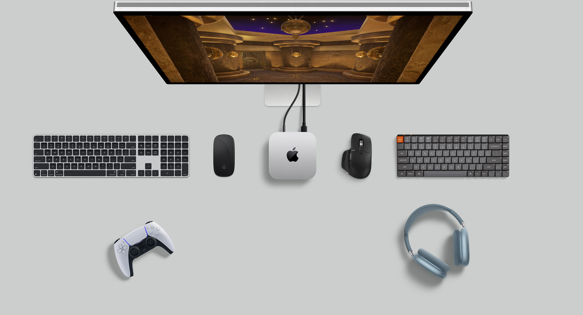 俯視圖展示銀色 Mac mini 擺放在桌上，旁邊放有一部顯示器、無線鍵盤、無線滑鼠、一個遊戲手掣，以及 AirPods Max。