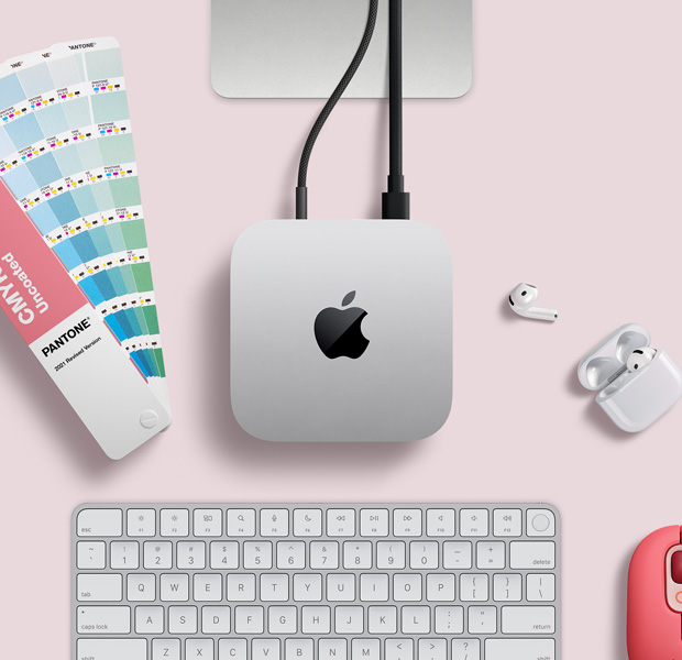 俯視圖展示銀色 Mac mini 擺放在桌上，旁邊放有 AirPods、一個粉紅色無線鍵盤、粉紅色無線滑鼠，以及一疊扇狀顏色卡。