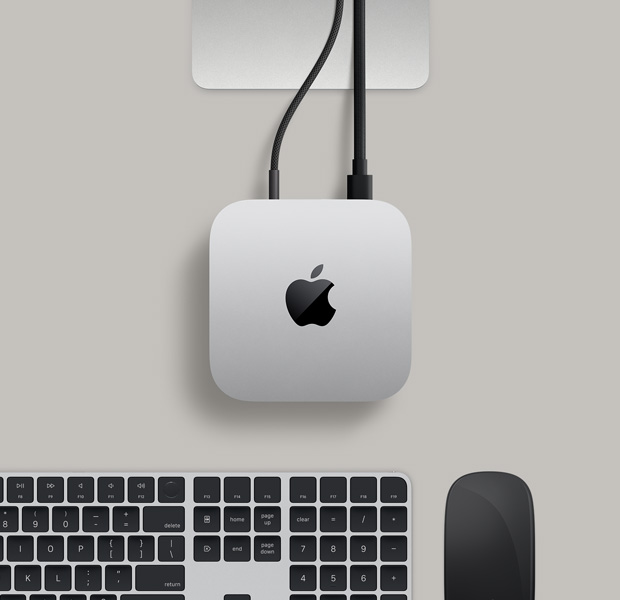 銀色 Mac mini 俯視圖，兩條連接線從背面插口連接至一部顯示器，旁邊放有黑色精妙滑鼠和黑色精妙鍵盤。