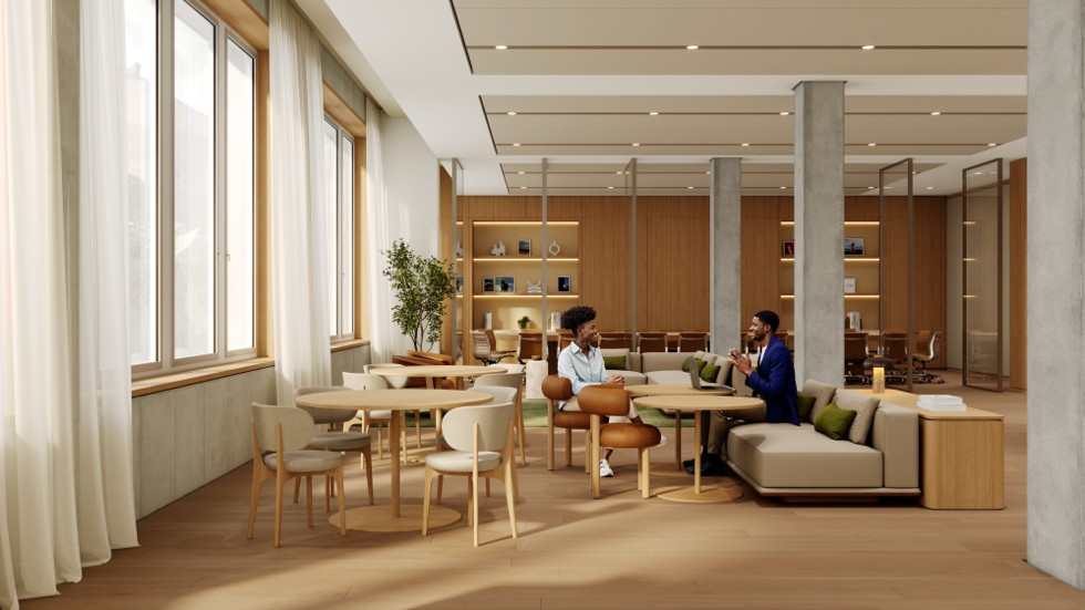 Several people are gathered in a modern, brightly lit break area with wooden furniture, including tables, chairs, and a comfortable couch.