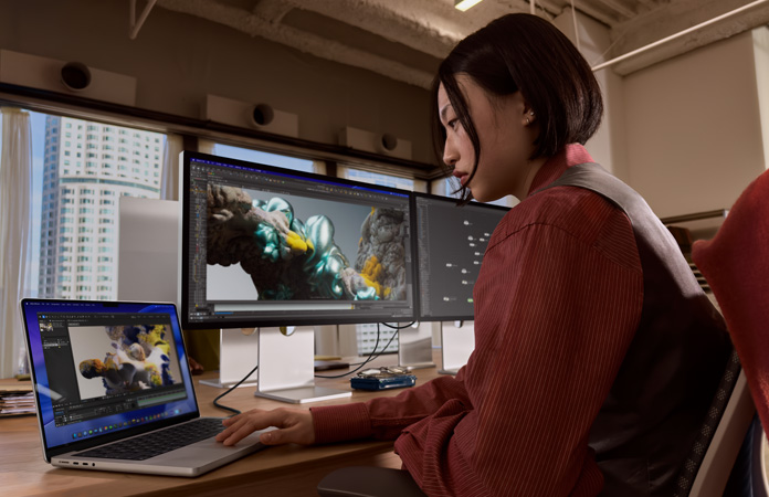 Osoba pracuj?ca w biurze na MacBooku Pro pod??czonym do monitora Studio Display XDR