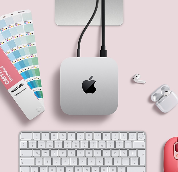 AirPods, pembe bir kablosuz klavye, pembe bir kablosuz mouse ve a??k duran bir renk kartelas? ile birlikte masa düzeninde yer alan gümü? rengi Mac mini'nin üstten g?rünümü