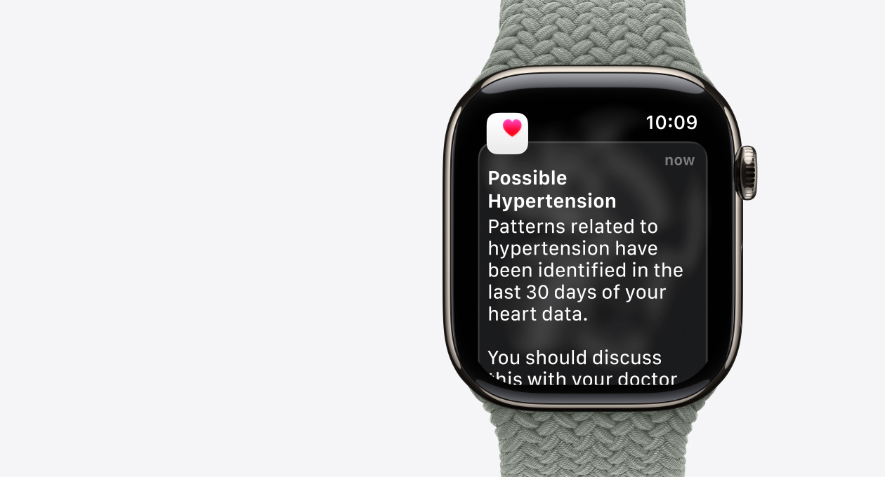 Apple Watch Series 11, dabīga krāsa, titāna ietvars, pazi?ojums par iespējamu hipertensiju, rozā sirsni?a baltā laukumā, labais sāns, Digital Crown, siksni?a, pelēkza?a Braided Solo Loop