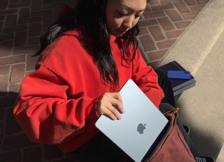 Iemand die op stenen trappen zit en een MacBook in een rugzak stopt.