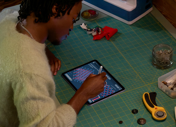 Iemand die een illustratie maakt met Apple Pencil op iPad, zittend op een groene snijmat met naaigerei.