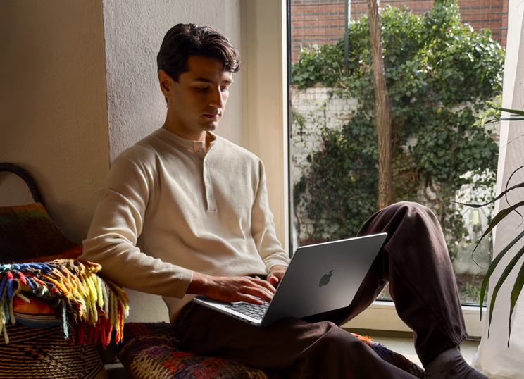 Uma pessoa sentada no ch?o usando um MacBook ao lado de uma janela