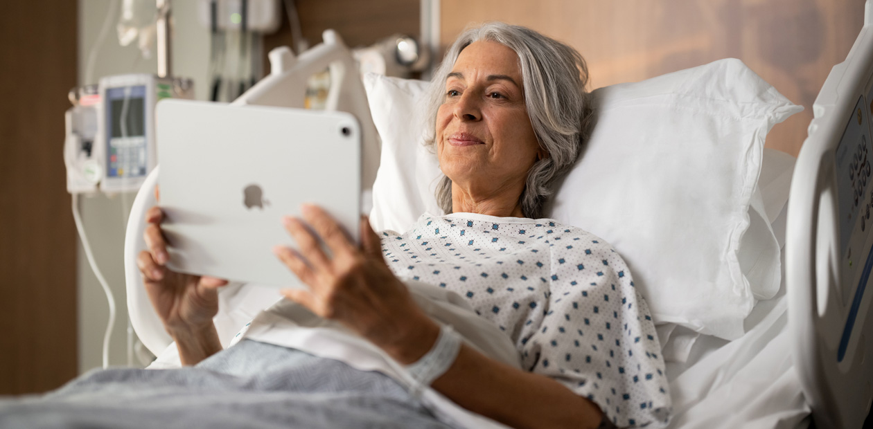 En kvindelig patient ligger i en hospitalsseng, mens hun kigger p? sin iPad.