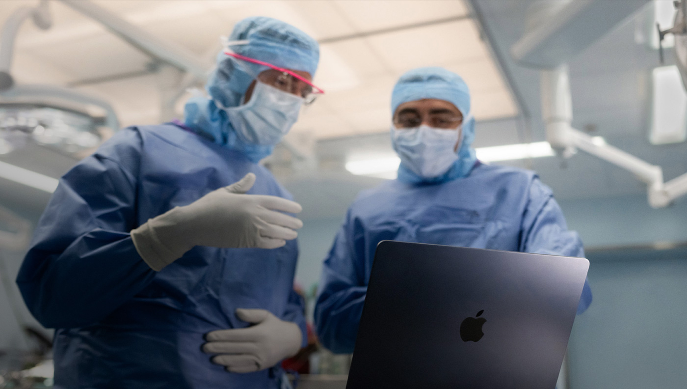 Dois cirurgi?es conversando sobre algo na tela de um MacBook Pro na sala de cirurgia.