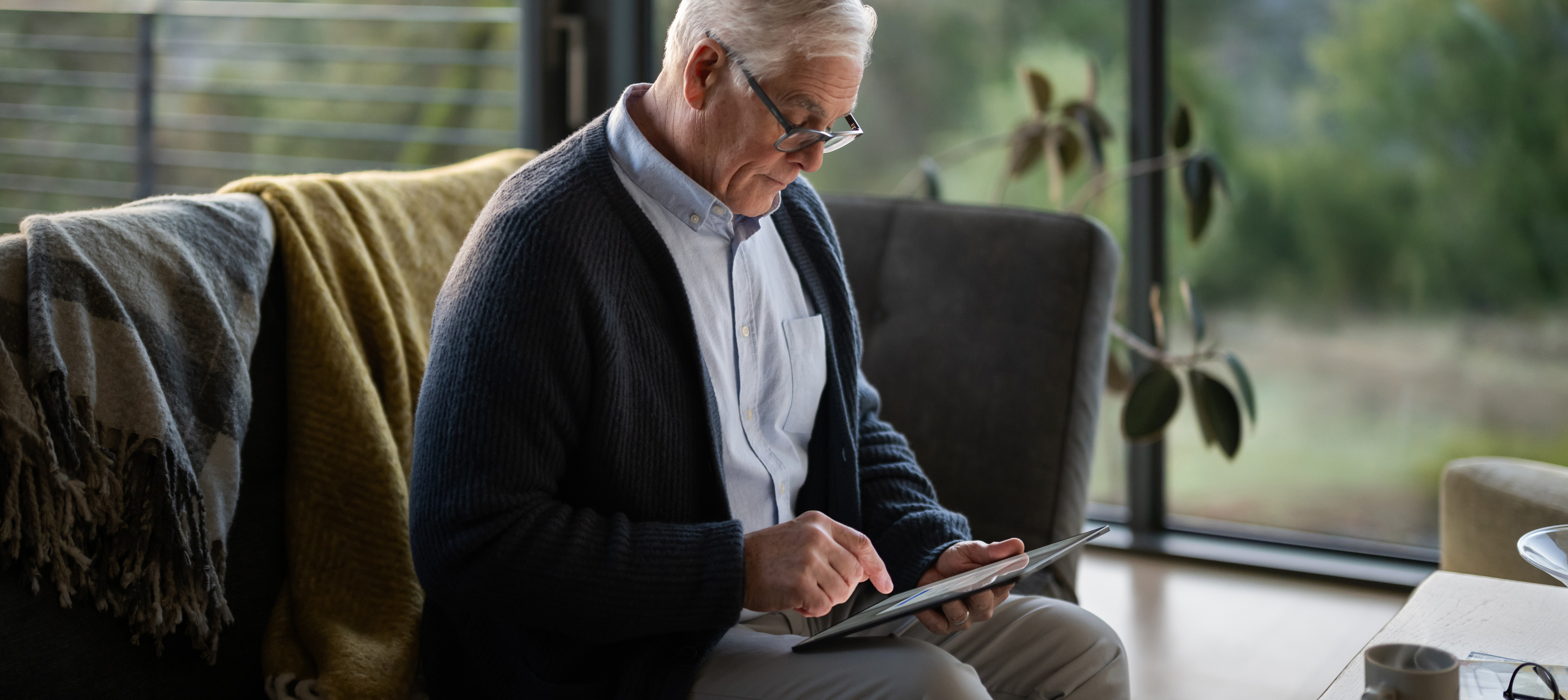 En ?ldre mand sidder p? en sofa og kigger p? en iPad.