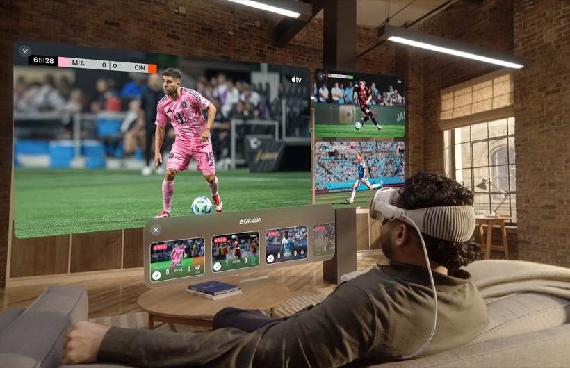 Apple Vision Proを裝著した人物がリビングのソファに座っている。その目の前には大きなスクリーンでビデオが表示され、その橫に2つの小さなスクリーンがある。それぞれ異なるスポーツイベントが映し出されている。大きなスクリーンの下には「さらに追加」と上部に書かれた選択ウィンドウが表示されている