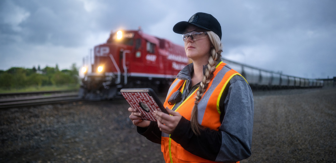 Eine Bahnmitarbeiterin h?lt ein iPad in der Hand und schaut auf die Gleise, w?hrend ein Zug vorbeif?hrt