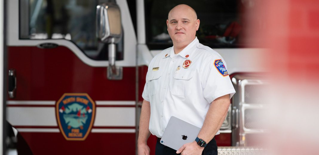 Der Feuerwehrchef steht vor einem Feuerwehrauto, h?lt ein iPad und tr?gt eine Apple Watch