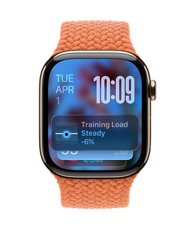 Une Apple Watch or rose avec un Bracelet tressé tangerine, le cadran affiche la date en haut à gauche, l’heure en chiffres superposés en haut à droite, le widget Charge d’entra?nement en bas, le tout en Liquid Glass translucide