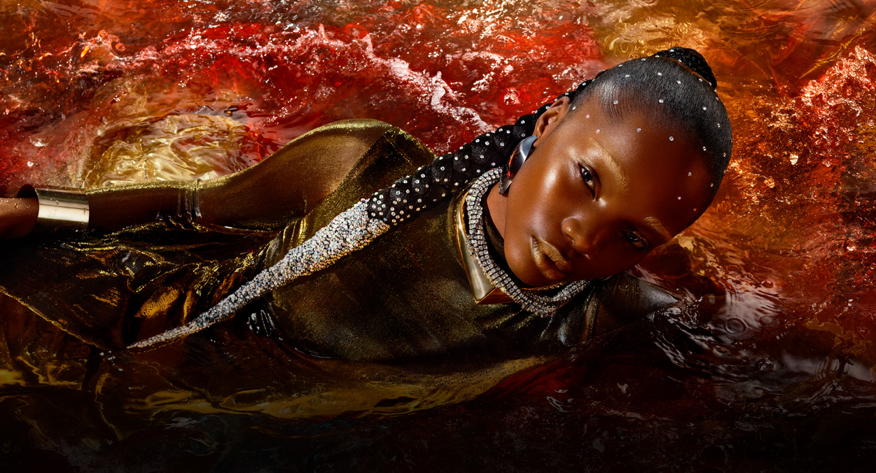 Image d’une personne vêtue d’une robe or métallique allongée sur le c?té dans une piscine d’eau rouge, illustrant la luminosité, le contraste et la gamme de couleurs étendue du Studio Display XDR