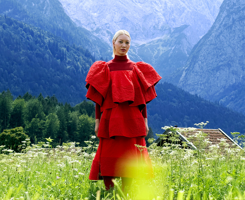 Une personne vêtue d’une robe rouge vif se tenant debout dans une vallée entourée de montagnes, illustrant la gamme de couleurs étendue du Studio Display XDR