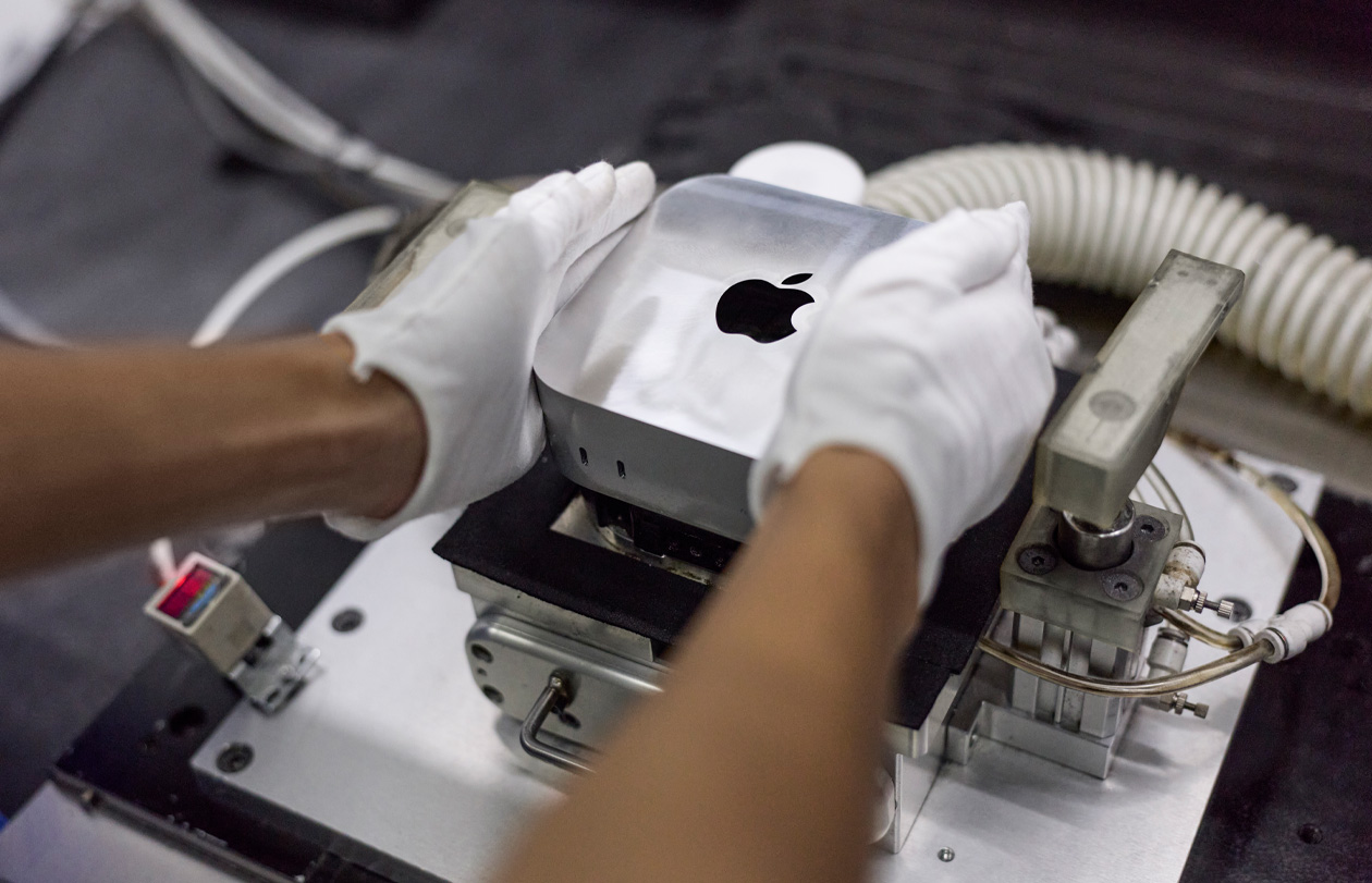 H?nder i handsker l?gger en Mac mini ned i en produktionsmaskine under samleprocessen