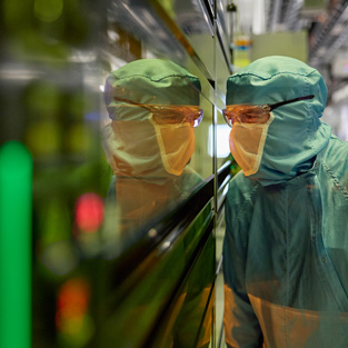 En medarbejder i fuld arbejdsdragt kigger ind i et vindue p? en halvledermaskine